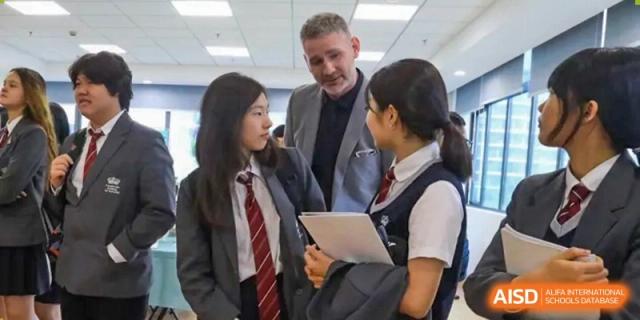 A male teacher from The British School of Nanjing talking with two female students in school uniform.