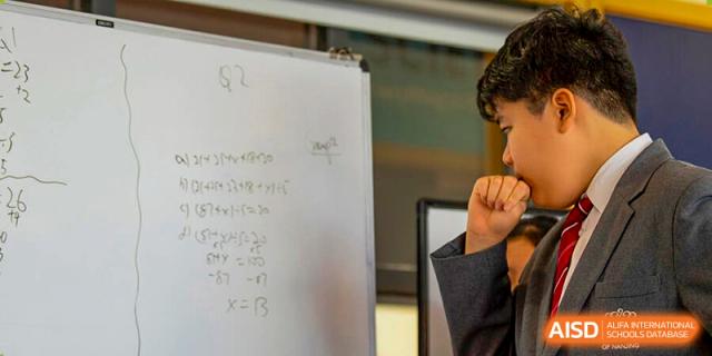 A male student from The British School of Nanjing standing in front of a whiteboard with mathematical equations.