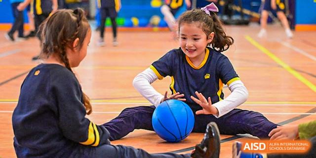 A smiling student from The British School of Nanjing sitting on a gymnasium floor with a blue basketball.