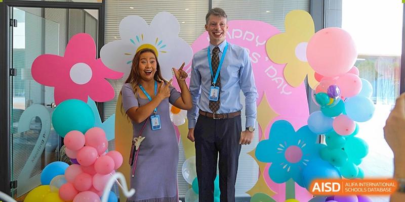 A male teacher and a female teacher from The British School of Nanjing smiling and posing for a photo in front of a colorful backdrop.