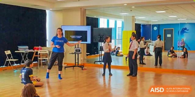 Two students from The British School of Nanjing engaged in an indoor sports activity with a coach and a large screen.