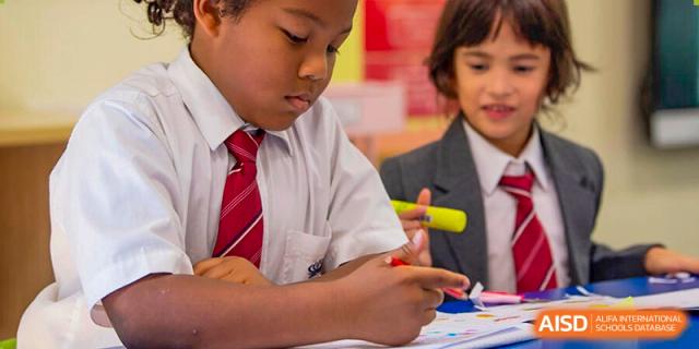 A male student from The British School of Nanjing in a white shirt and a red and white striped tie, writing with a highlighter in a classroom.