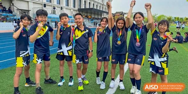 A group of smiling students from The British School of Nanjing with medals, cheering and raising their hands.