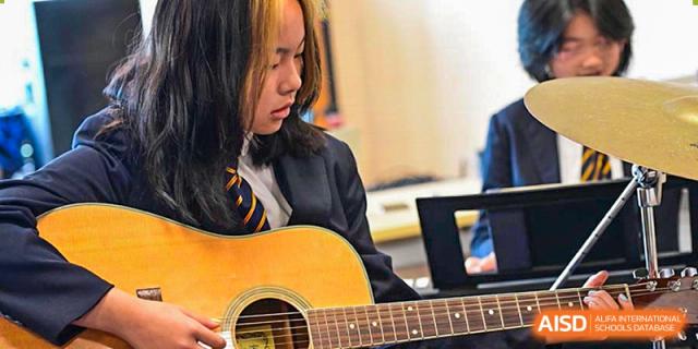 A female student from The British School of Nanjing playing an acoustic guitar indoors.