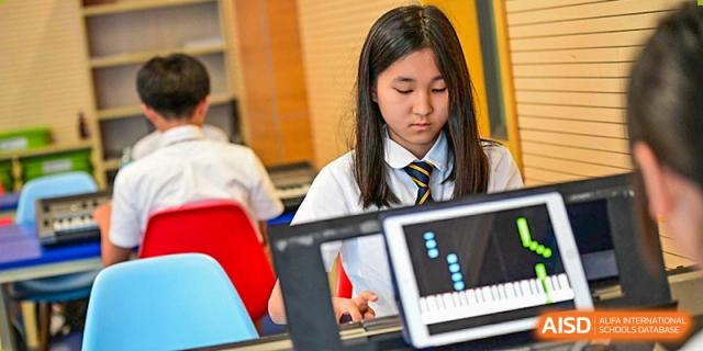 A female student from The British School of Nanjing with a yellow striped tie and a laptop, concentrating on her work.