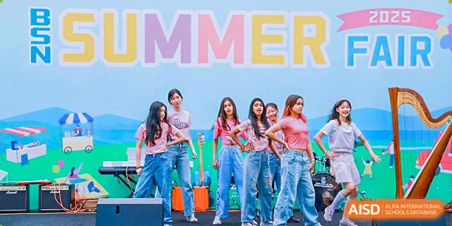 A group of female students from The British School of Nanjing in matching blue jeans and colorful tops, posing with props.