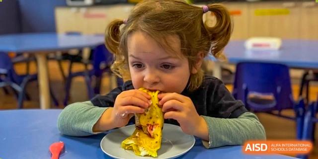 A young child from The British School of Nanjing with curly hair, taking a bite of food.