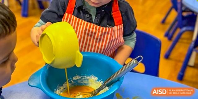 A young child from The British School of Nanjing wearing an apron, pouring a yellow mixture into a blue bowl.