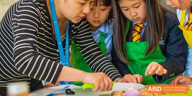 A group of students from The British School of Nanjing wearing green aprons, working together on a food preparation project.