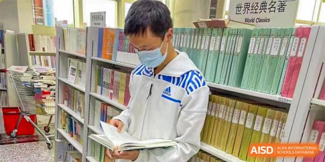 A student from The High School Affiliated To Beijing Normal University wearing a mask and reading a book in the school library.