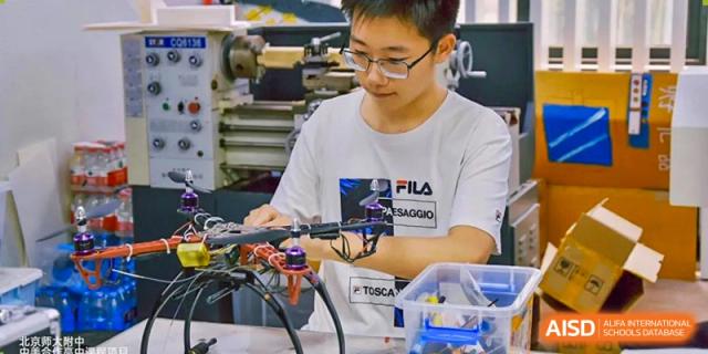 A student from The High School Affiliated To Beijing Normal University wearing safety glasses and working on a robotics or electronics project.