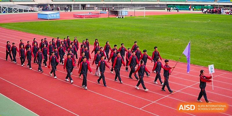 Students from The High School Affiliated To Beijing Normal University marching on a red track during a sports event.