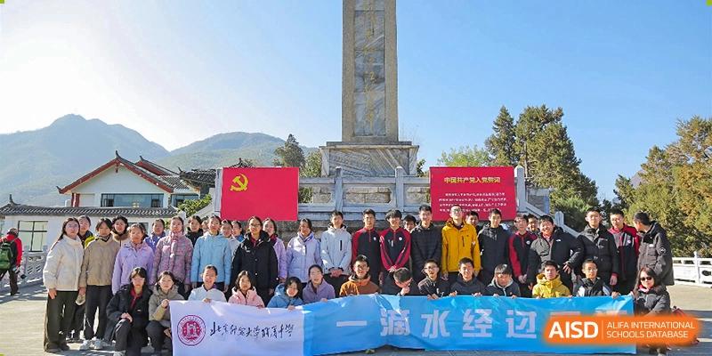 A group of students and faculty from The High School Affiliated To Beijing Normal University gathered outdoors with a monument in the background.