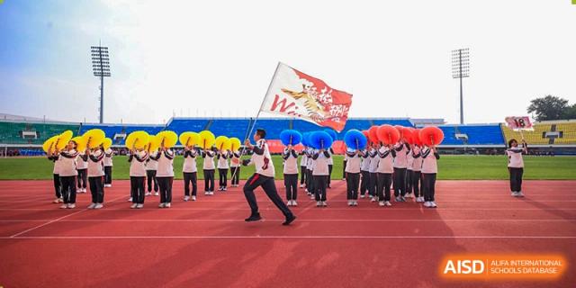 Students and faculty from The High School Affiliated To Beijing Normal University holding banners and cheering during a ceremony.