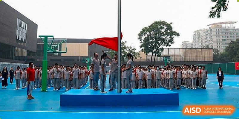 A group of students from The High School Affiliated To Beijing Normal University standing on a podium with a large flag and banners.