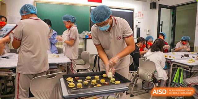 A student from The High School Affiliated To Beijing Normal University, wearing a mask and apron, placing food on a grill.