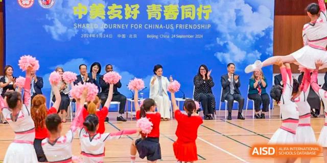 Students and faculty from The High School Affiliated To Beijing Normal University sitting on a stage at an event with a banner that reads 'Friendship' in the background.
