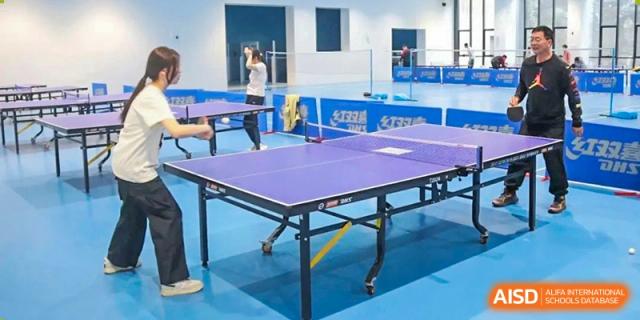 Students from The High School Affiliated To Beijing Normal University playing table tennis in a gymnasium.