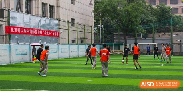 A group of students from The High School Affiliated To Beijing Normal University playing soccer on an outdoor field.