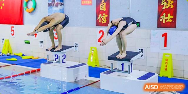 Students from The High School Affiliated To Beijing Normal University practicing diving or swimming at an indoor pool.