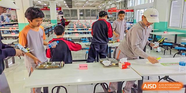 Students and faculty from The High School Affiliated To Beijing Normal University at tables in a cafeteria or large dining hall.