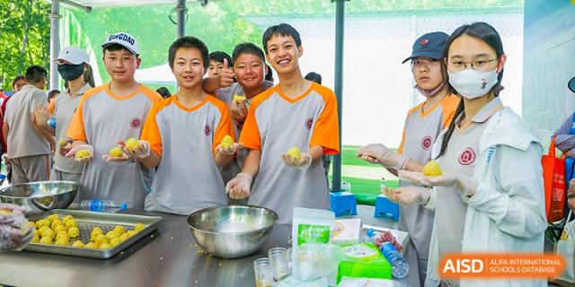 A group of smiling students from The High School Affiliated To Beijing Normal University in a kitchen, preparing food.