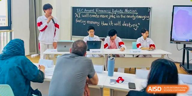 A male teacher from The High School Affiliated to Renmin University of China, Tongzhou Campus, sits at a desk in a classroom.