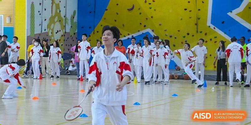 A student from The High School Affiliated to Renmin University of China, Tongzhou Campus, in a red and white tracksuit, plays badminton.