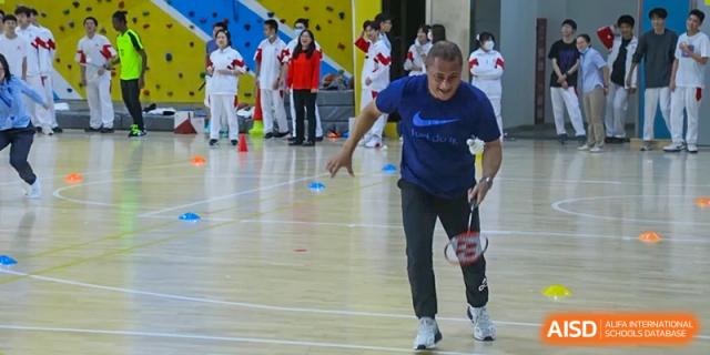 A student from The High School Affiliated to Renmin University of China, Tongzhou Campus, in a blue shirt and gray pants, runs while playing badminton.