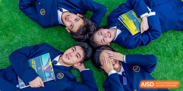 Students from Tianfu school The Integrated and Innovative Curriculum lying on a grassy field and smiling at the camera.