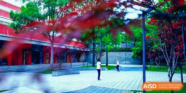 A student from Tianfu school The Integrated and Innovative Curriculum walking on a stone path with red walls and trees in the background.