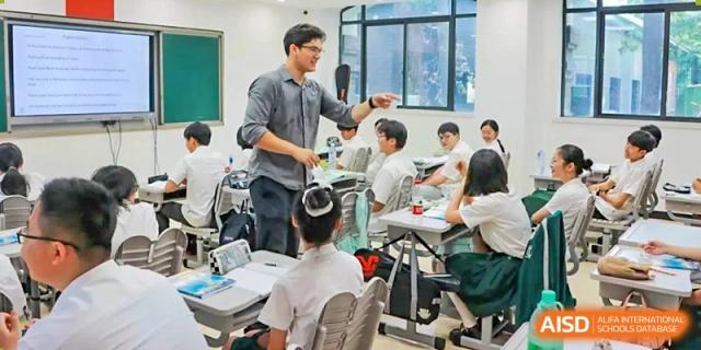 A teacher from Times College interacting with a student and a group of students in a classroom.