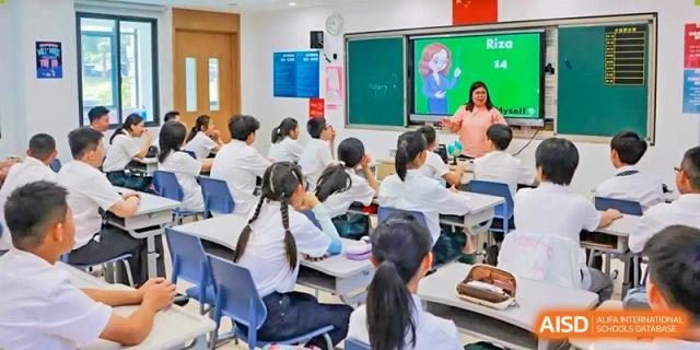 A teacher from Times College standing in front of the class and pointing to the interactive whiteboard.