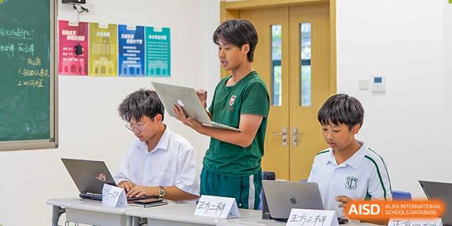 A student from Times College holding a laptop and giving a presentation in a classroom.