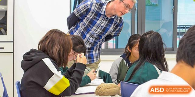 A teacher from Times College helping students with their work at their desks.