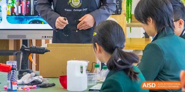 A teacher from Times College helping a student with a project in a workshop setting.