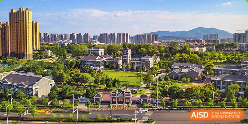 An aerial view of the Times College campus with modern buildings and sports fields, surrounded by a city skyline and mountains in the distance.