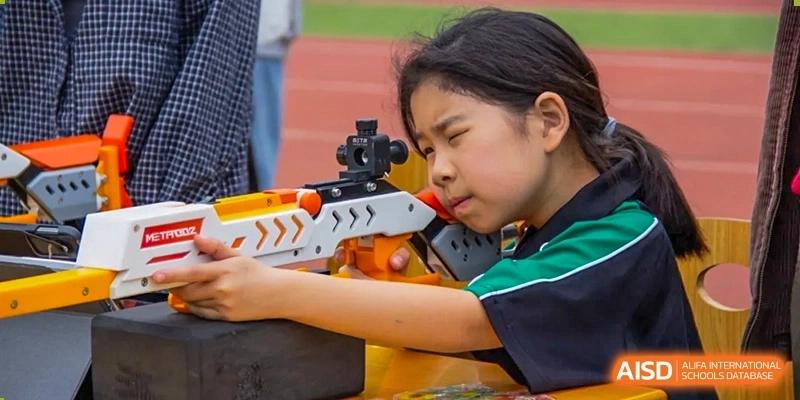 A young student from Times College aiming a toy rifle during an activity.