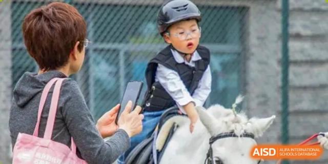 A young student from Times College wearing a helmet and vest while riding a horse.