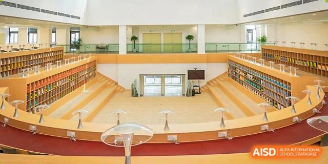 A large, empty UWC Changshu China auditorium with tiered seating made of wood, and two light-colored stages.