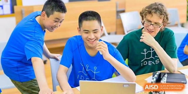 A UWC Changshu China student in a blue t-shirt smiling while using a laptop.