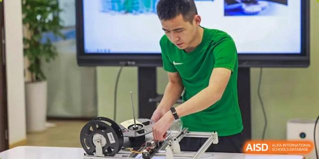 A young male student from UWC Changshu China in a green shirt is focused on assembling a technical device in a classroom.