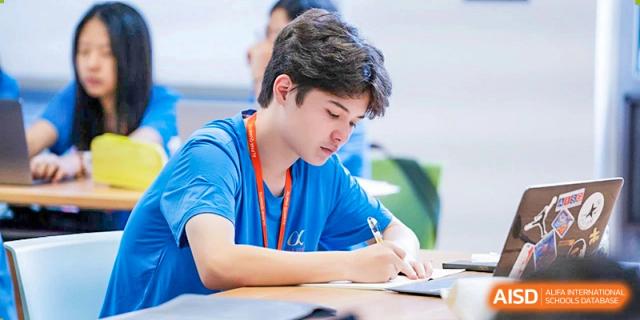 A UWC Changshu China student with a camera strap around his neck writing in a notebook.