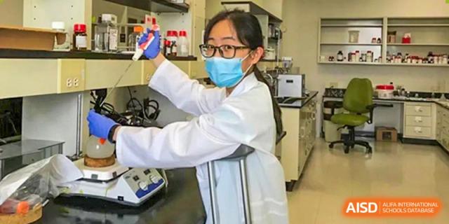 A UWC Changshu China student wearing a lab coat and mask, holding a beaker in a science lab.