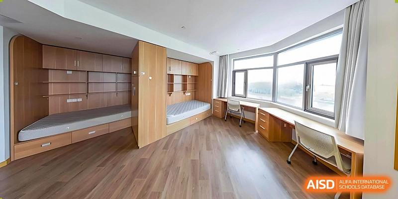 A wide-shot of a dorm room with a bed and a study desk by a large window at UWC Changshu China.