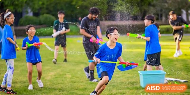 A male student, wearing goggles and a blue shirt, runs with a water gun in a playful outdoor activity at UWC Changshu China.