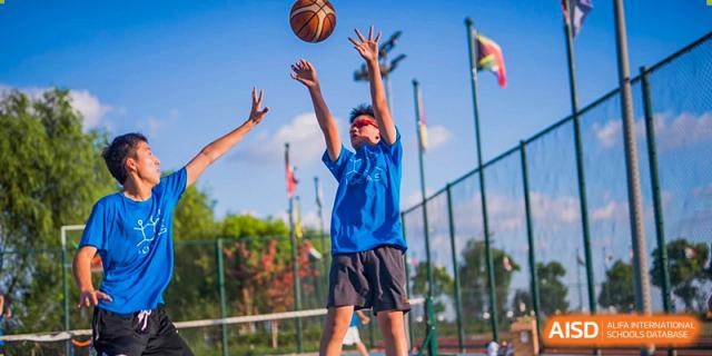 A male student in a blue shirt jumps to block a shot during a basketball game at UWC Changshu China.