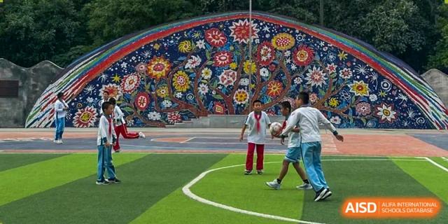 Students play soccer on a sports field next to a large, colorful mosaic mural at UWC Changshu China.