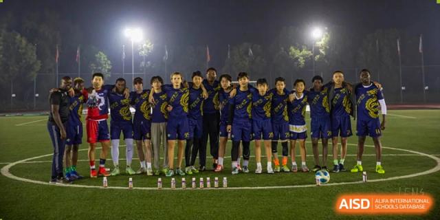 A group of UWC Changshu China students in matching dark blue and yellow uniforms standing together on a soccer field at night.