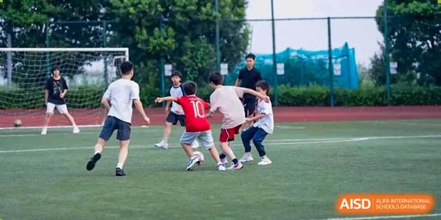 UWC Changshu China students playing soccer on a grassy field, with a student in a red shirt dribbling the ball.